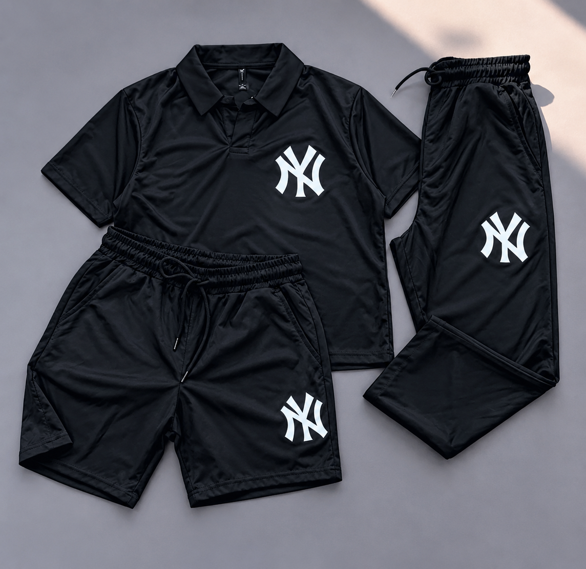 A three-piece black athletic loungewear set featuring a short-sleeve polo shirt, shorts, and pants, all with white New York Yankees 'NY' logos. The set is laid out flat on a gray background.