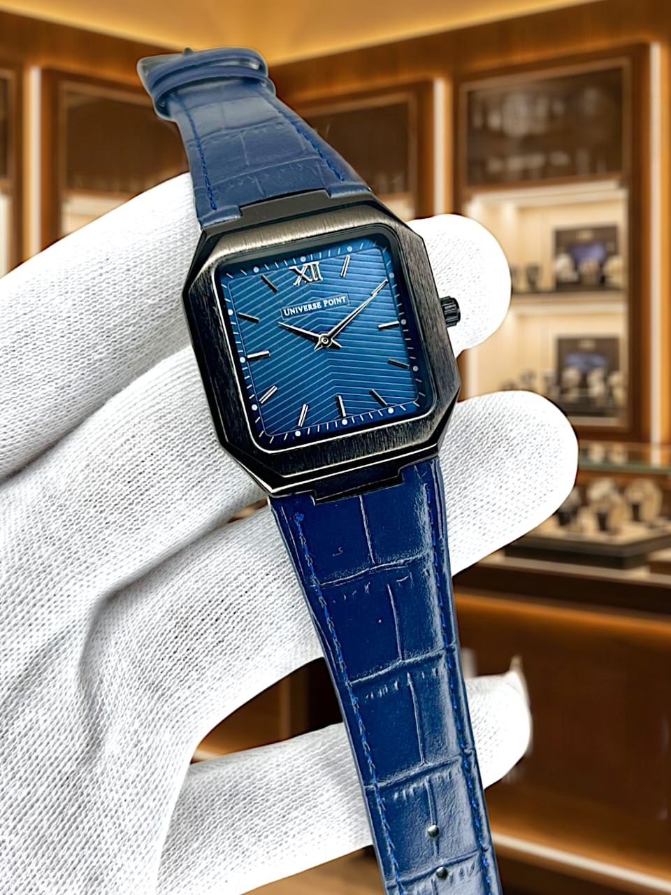 Blue wristwatch with a detailed face held by a white glove against a blurred background.